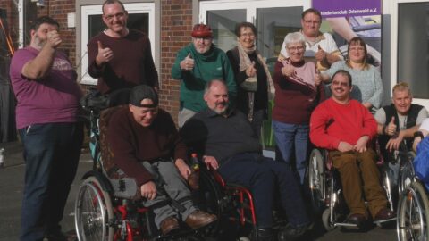 Menschen mit und ohne Rollstuhl stehen im Kreis vor dem DWO.